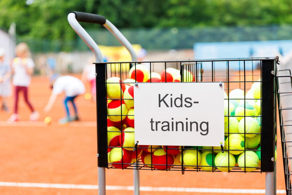 Basket cart filled colorful tennis balls sign plate Kids-training clay tennis court children playing training background. Summer sport camp. Sports youth school. Healthy child kid active lifestyle